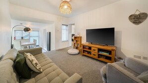 A living room with a sofa, a TV, and a bookshelf. - Roll-top bath, rain shower and space for 8 in the heart of Filey (North Yorkshire)