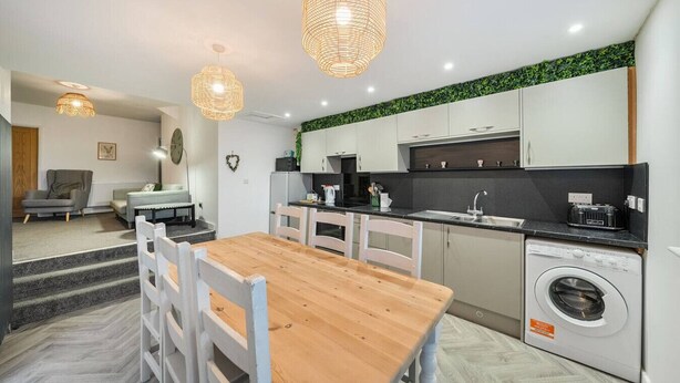 A compact kitchen with a wooden dining table, white chairs, a washing machine, and a sink. - Roll-top bath, rain shower and space for 8 in the heart of Filey (North Yorkshire)