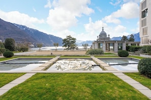 Ein Innenhof mit einem zentralen Brunnen, ein Gebäude mit einer Kuppel und Berge im Hintergrund.