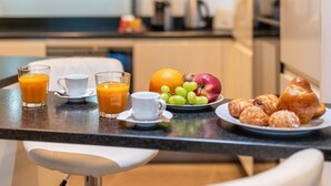 Taula de l'esmorzar amb suc d'aranja, cafè i pastissos en una cuina moderna amb armaris blancs i una campana extractora d'acer inoxidable.