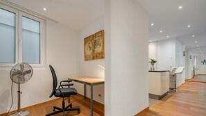 Un espai d'oficina modern amb escriptori de fusta, cadira d'oficina negra i ventilador de peu.