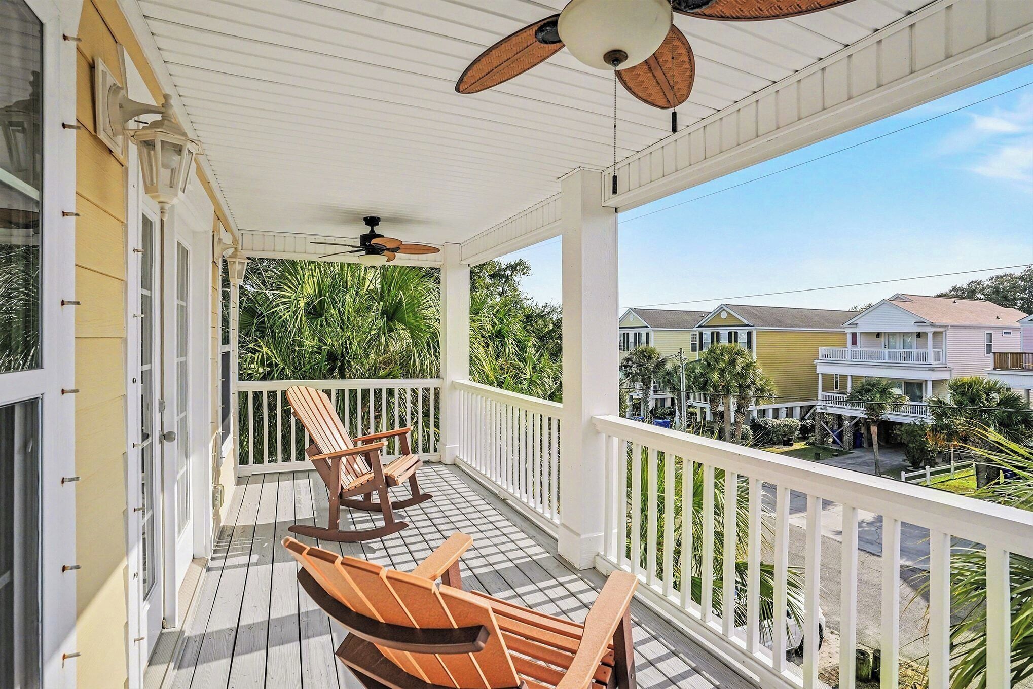 A covered porch with wooden chairs, a ceiling fan, and a view of neighboring houses.