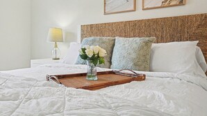 Una cama bien hecha con una bandeja, almohadas y un florero.