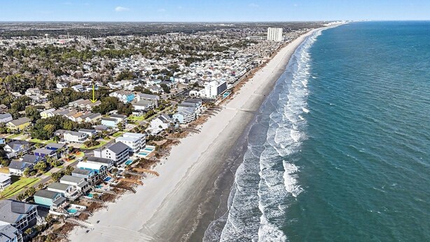Vista aérea de una zona residencial costera con casas, una playa y un océano azul y despejado.