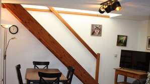 Un salon chaleureux avec un escalier en bois, une table à manger avec des chaises, un canapé, un téléviseur et une horloge au mur.