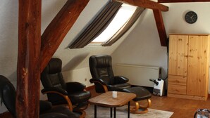Une pièce de style « loft », avec des poutres en bois apparentes, une grande fenêtre, un meuble en bois et des fauteuils en cuir.
