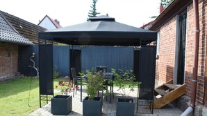 Un patio couvert avec une table et des chaises, des plantes en pot et un mur en briques.
