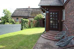 A brick house with a thatched roof, a wooden door, and a small porch with two chairs.