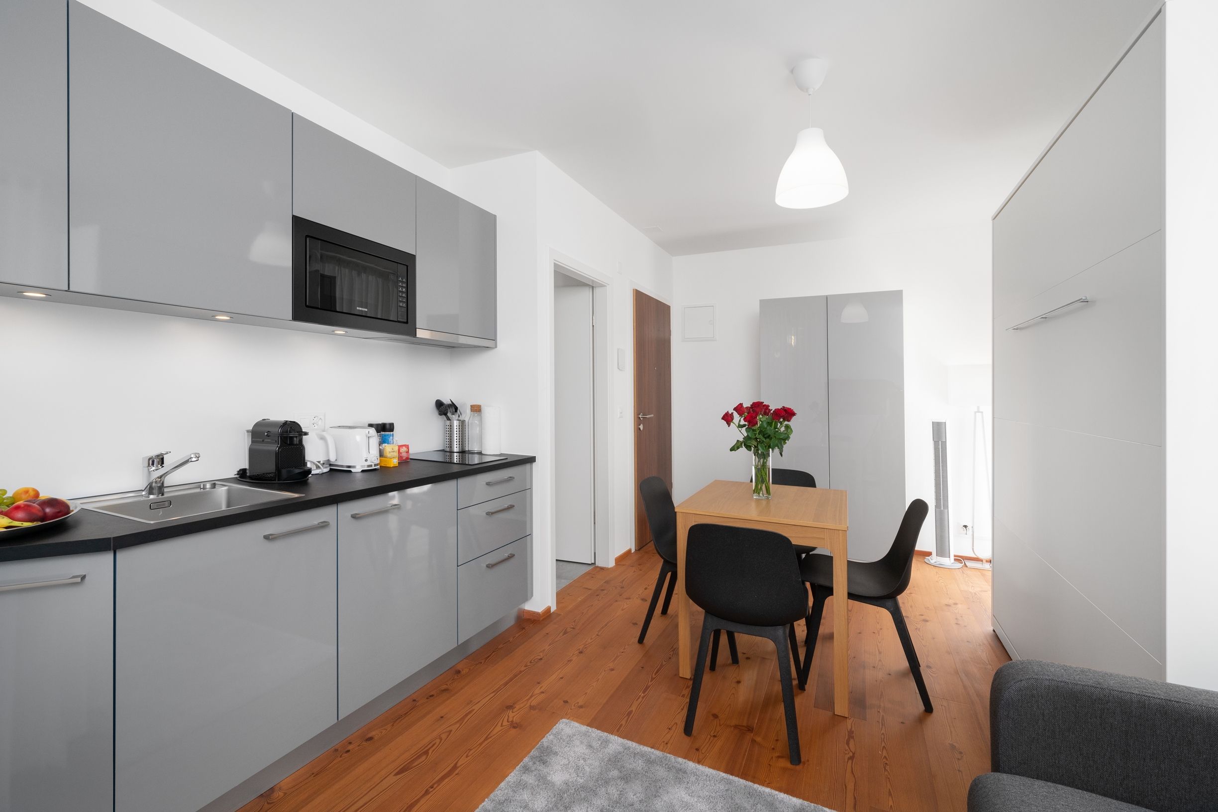 Une cuisine moderne avec des meubles gris, un micro-ondes noir et une table à manger en bois avec des chaises noires.