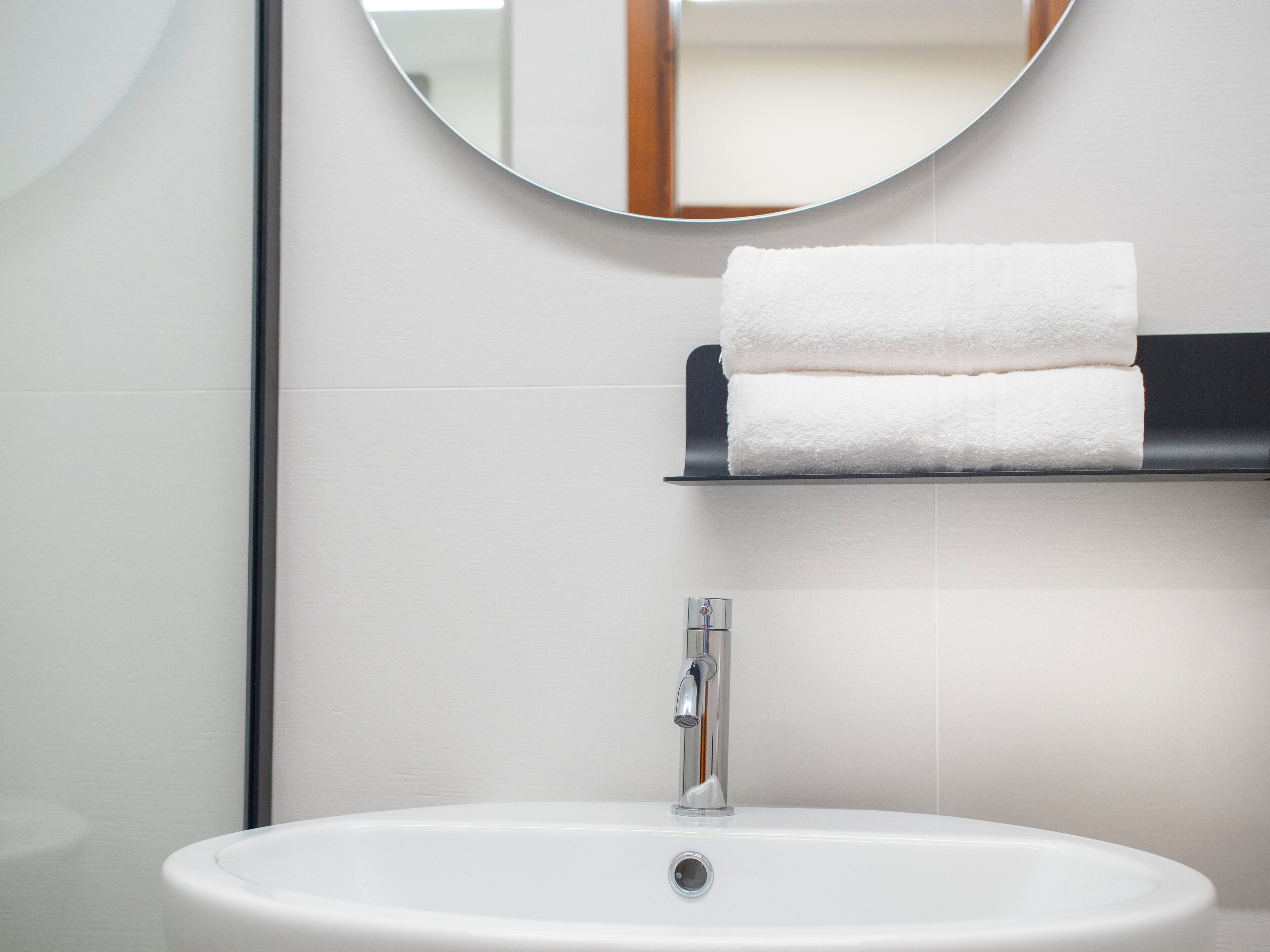 A bathroom with a white sink, a round mirror, and a towel rack with two folded towels.