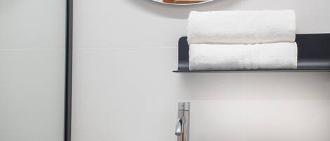 A bathroom with a white sink, a round mirror, and a towel rack with two folded towels.
