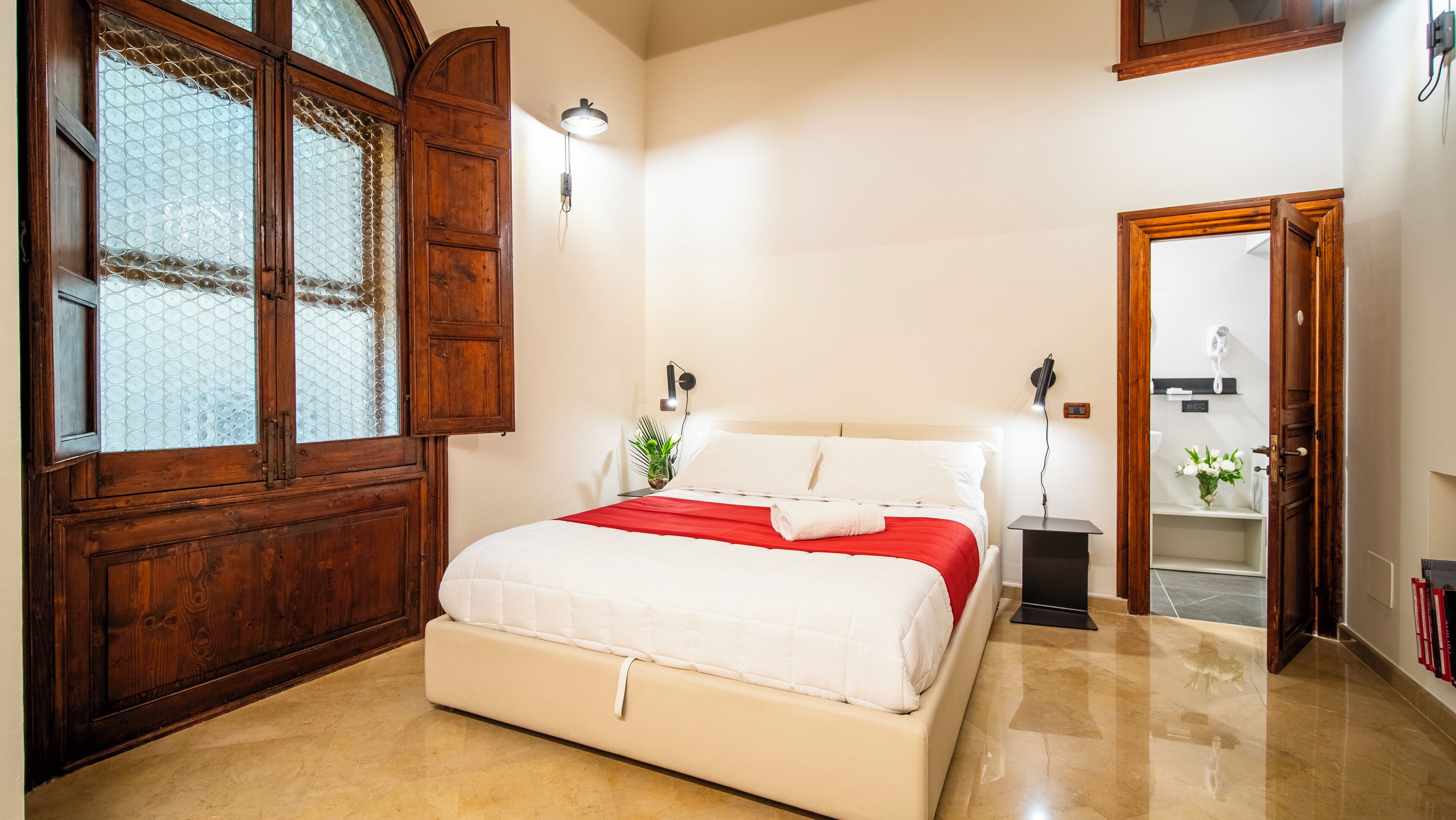 A bedroom with a bed, wooden wardrobe, and a bathroom visible through an open door.