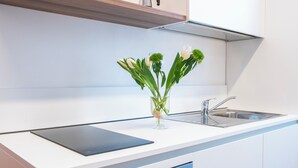 Ett modernt kök med en vit bänkskiva, en vas i glas med blommor och en svart surfplatta.
