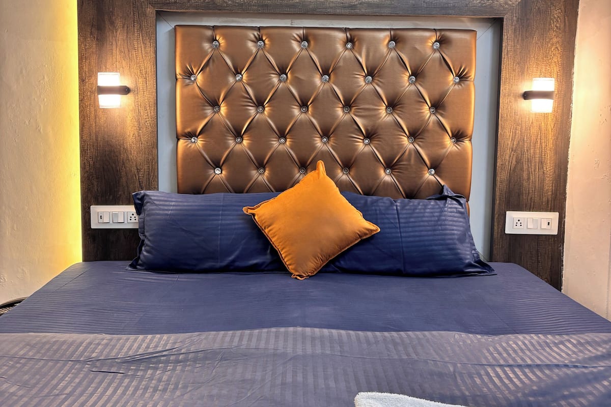 A bed with a tufted headboard, two bedside lamps, and a blue and orange pillow arrangement.