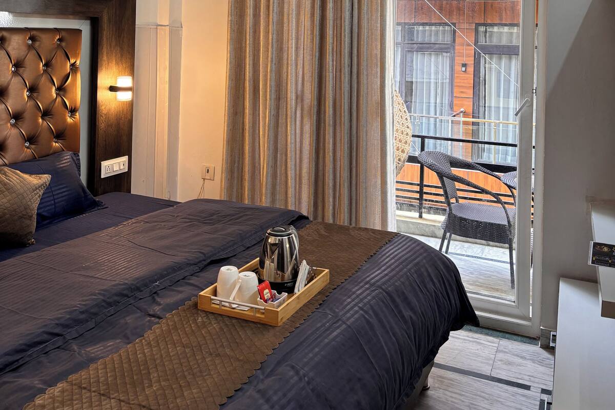 A hotel room with a bed, a ceiling fan, an air conditioning unit, a sliding glass door, and a balcony with a chair.