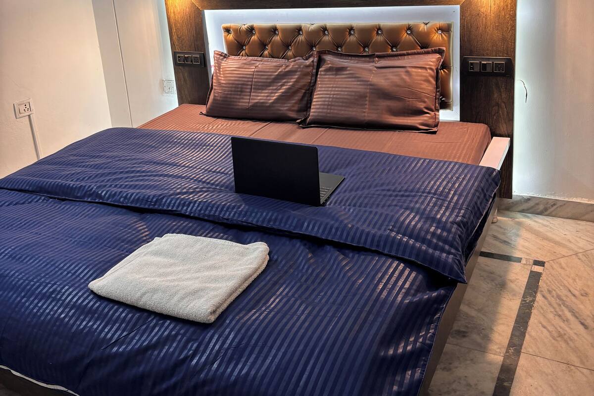 A neatly made bed with a laptop, a headboard with built-in lighting, and a bedside table.
