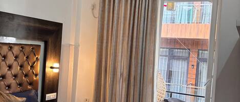 A hotel room with a tufted headboard, a bed with a dark blue bedspread, a tray with toiletries, and a view of the outside balcony.