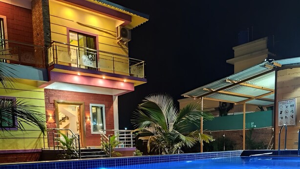 A swimming pool with a tiled edge, surrounded by a building with a balcony and a staircase leading to an upper level. - SeaBreeze Nature Embrace Villa - Alibaug (Nagaon)