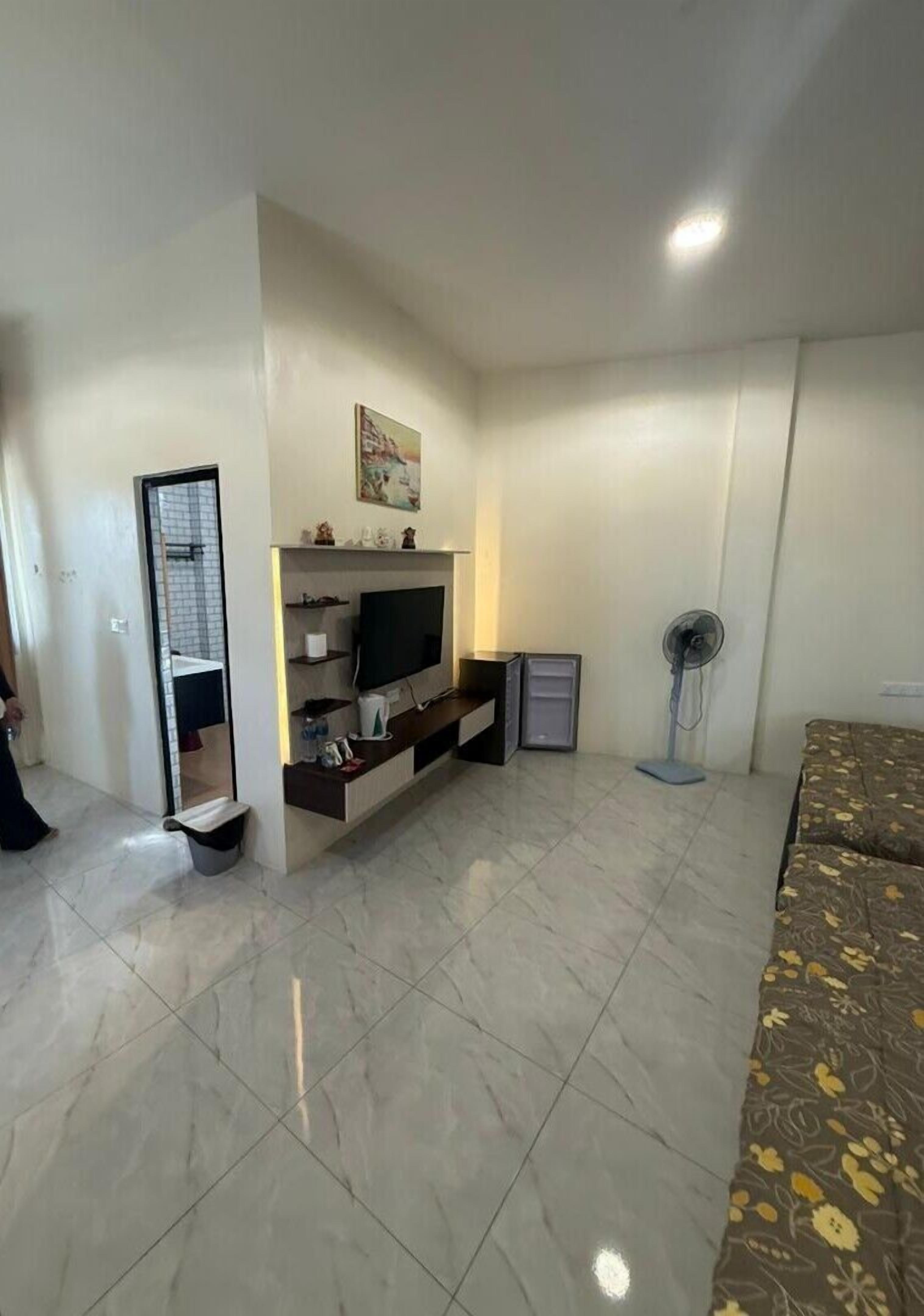 A living room with a flat-screen TV, a small cabinet, a fan, and a patterned sofa.