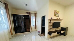 Un salón amplio con suelo de baldosas, un armario con puerta corredera de cristal, un televisor de pantalla plana sobre un mueble de madera y una pequeña estantería con objetos decorativos.