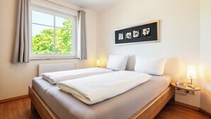Un letto matrimoniale con lenzuola bianche, un comodino con una lampada e una finestra con tende.