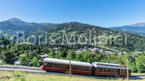 A train on tracks with a mountainous landscape in the background. - Apartment in Saint Gervais Near Cable Car (Saint-Gervais-les-Bains)