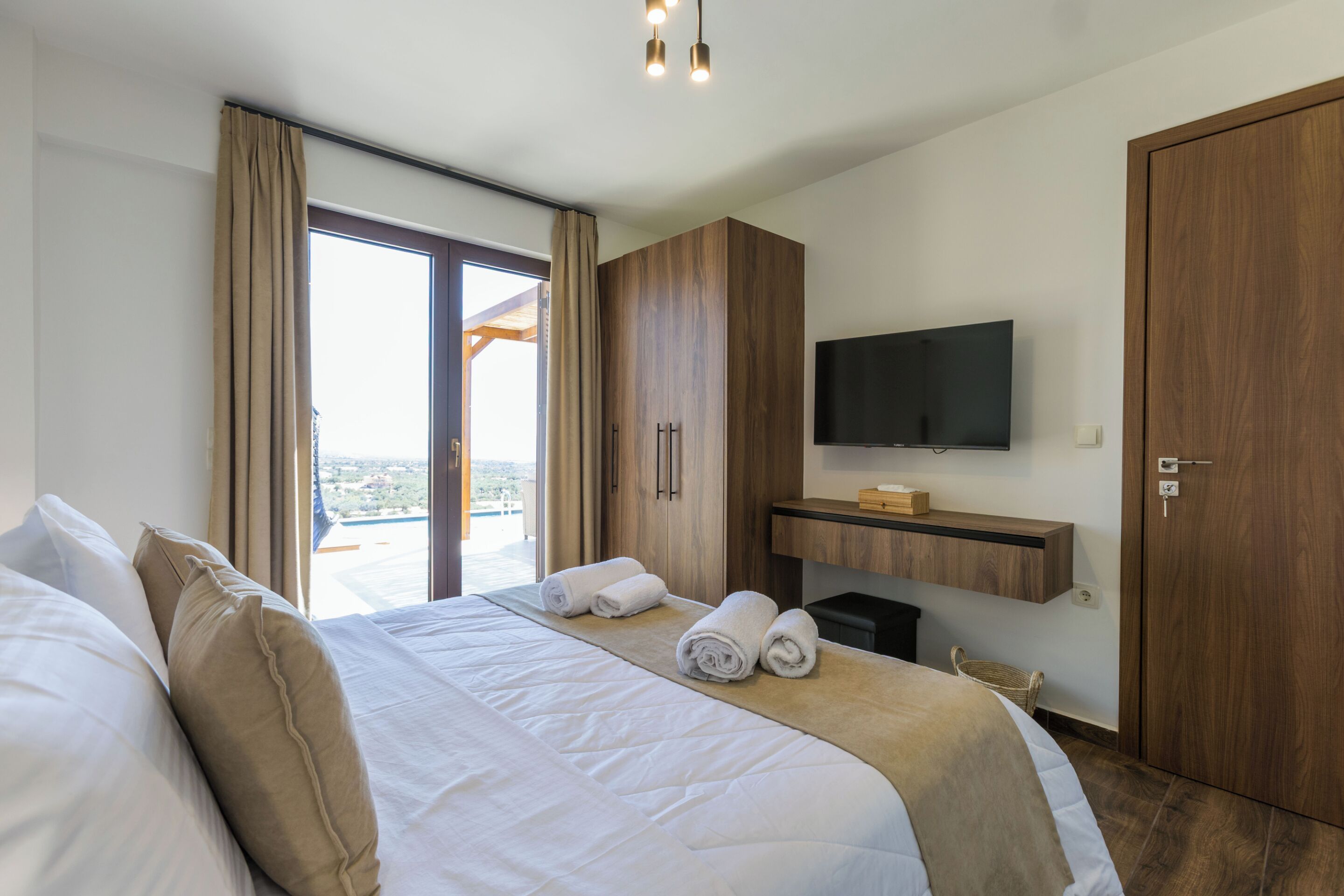 Een moderne hotelkamer met een groot bed, een flatscreen televisie aan de muur en een schuifdeur naar een balkon.