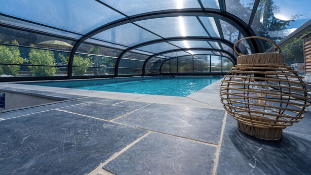 An indoor swimming pool with a clear glass ceiling, a stone floor, and a wicker basket on the right. - Description (Pléhédel)