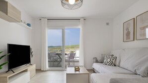 Una sala de estar moderna con una televisión de pantalla plana, un sofá, una mesa de centro y una puerta corrediza de vidrio que da a un patio exterior.