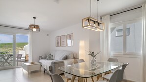 Una sala de estar moderna con una mesa de comedor de cristal, sillas grises, un sofá y un balcón con mobiliario exterior.