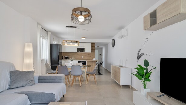 Una sala de estar moderna con sofá, mesa de comedor, sillas, televisor y una cocina al fondo.