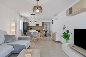 Una sala de estar moderna con sofá, mesa de comedor, sillas, televisor y una cocina al fondo.