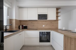 Una cocina moderna con armarios blancos, encimera de madera, microondas integrado y horno.