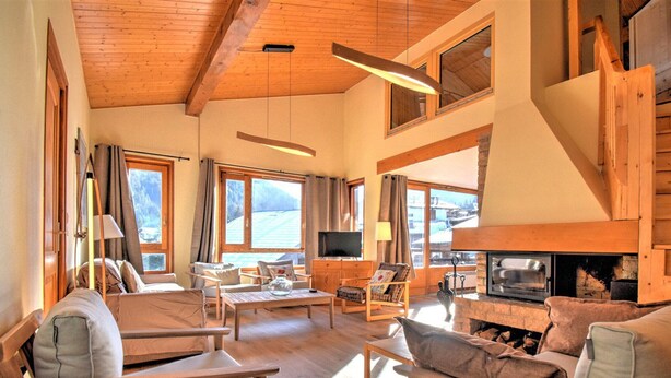 Ein geräumiges Wohnzimmer mit Holzmöbeln, einem Kamin und großen Fenstern mit Blick ins Freie.