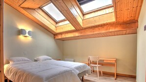 Ein Schlafzimmer mit Dachfenster, einem Bett, einem Sessel und einem Schreibtisch.