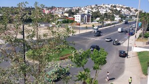 Una amplia vía con vehículos, un paso de peatones y un área residencial con colinas al fondo.