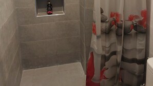 Zona de ducha con pared de azulejos grises, un estante pequeño con artículos de aseo y una cortina de ducha con estampado floral.