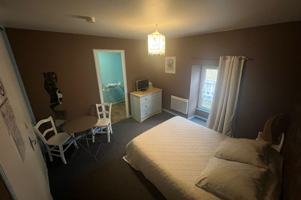 Une chambre à coucher avec un lit, un bureau, une chaise, une télévision et une fenêtre avec des rideaux.
