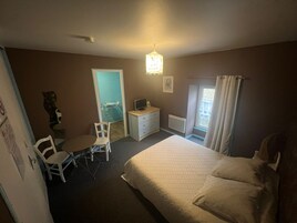 A bedroom with a bed, a desk, a chair, a television, and a window with curtains.