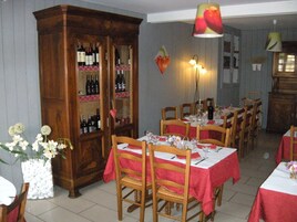 A dining area with wooden chairs and tables, a large wooden cabinet with wine bottles, and a wall-mounted light fixture.