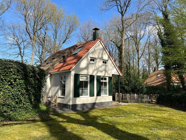 Ein eingeschossiges Haus mit schrägem Dach, weißen Außenwänden und grünen Fensterläden.