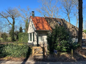 Ein kleines, eingeschossiges Haus mit rotem Ziegeldach, Schornstein und hölzernem Tor.