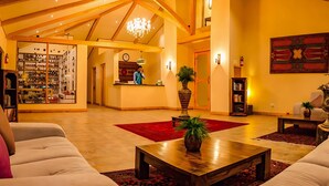 A spacious lobby with a high ceiling, wooden beams, a chandelier, a reception desk, and a large red rug. - The Villa Himalaya (Srinagar)