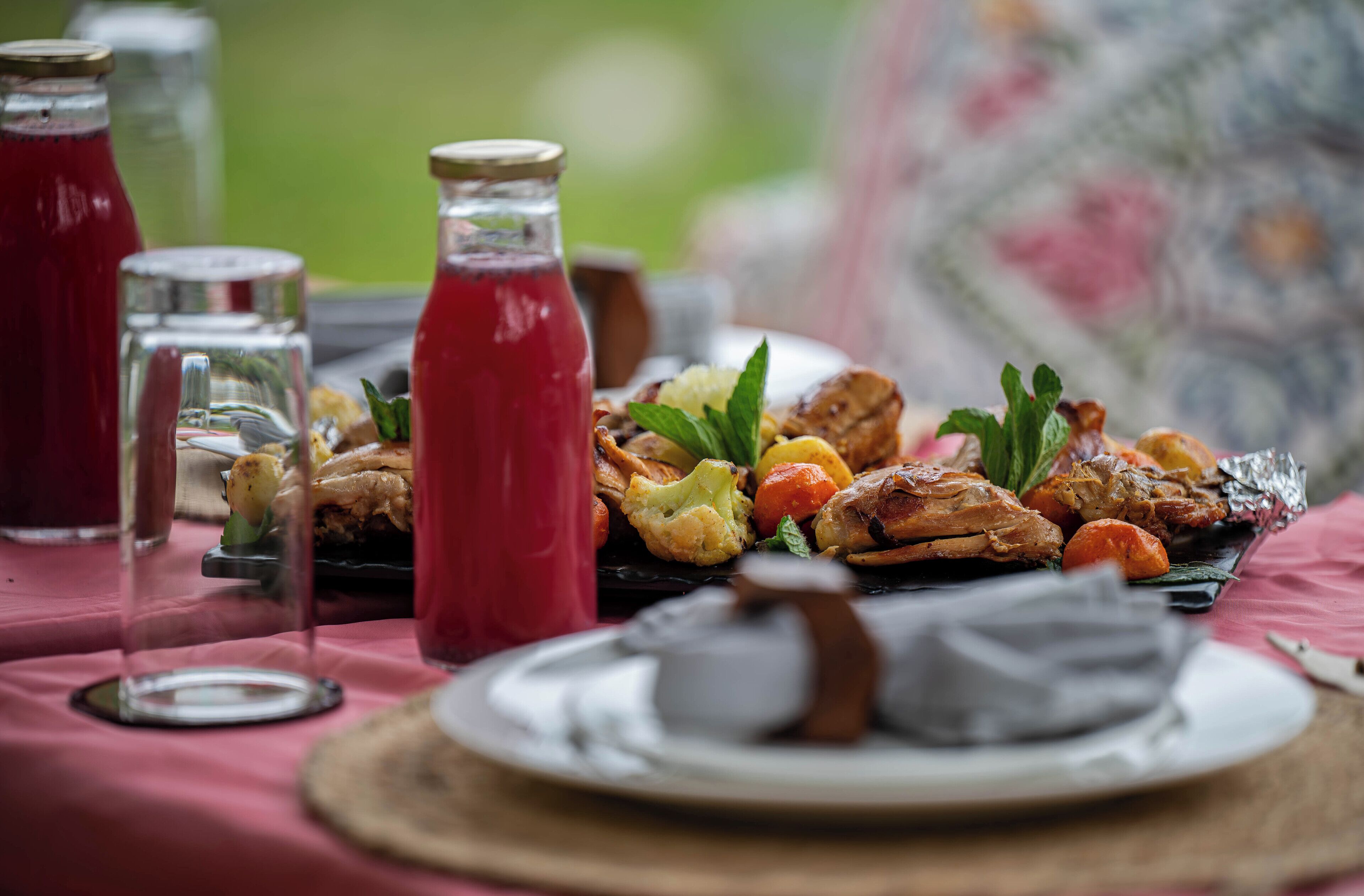 Egy asztal, amelyen különféle ételek találhatók, köztük sült húsok és zöldségek, valamint több üveg ital.
