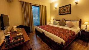 A hotel room with a wooden bed, a desk with a computer and a tray of snacks, a television, and a window with curtains. - The Villa Himalaya (Srinagar)