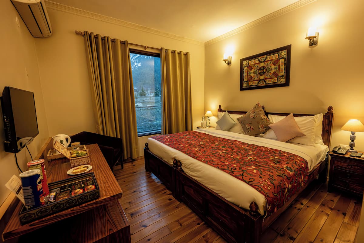 Habitación de hotel con cama de madera, un escritorio con computadora y una bandeja de bocadillos, televisión y ventana con cortinas.