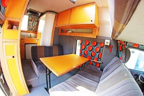 Ein kompaktes Wohnmobil-Interieur mit einer Küchenzeile, einem Esstisch und einer Sitzecke mit gemusterten Kissen.