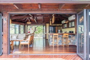 A spacious living area with a wooden floor, a seating area with a sofa and chairs, a kitchen with a stone countertop, and a view of the outdoors. - 3 chambres privées avec panorama sur le Morne (Grande Riviere Noire)