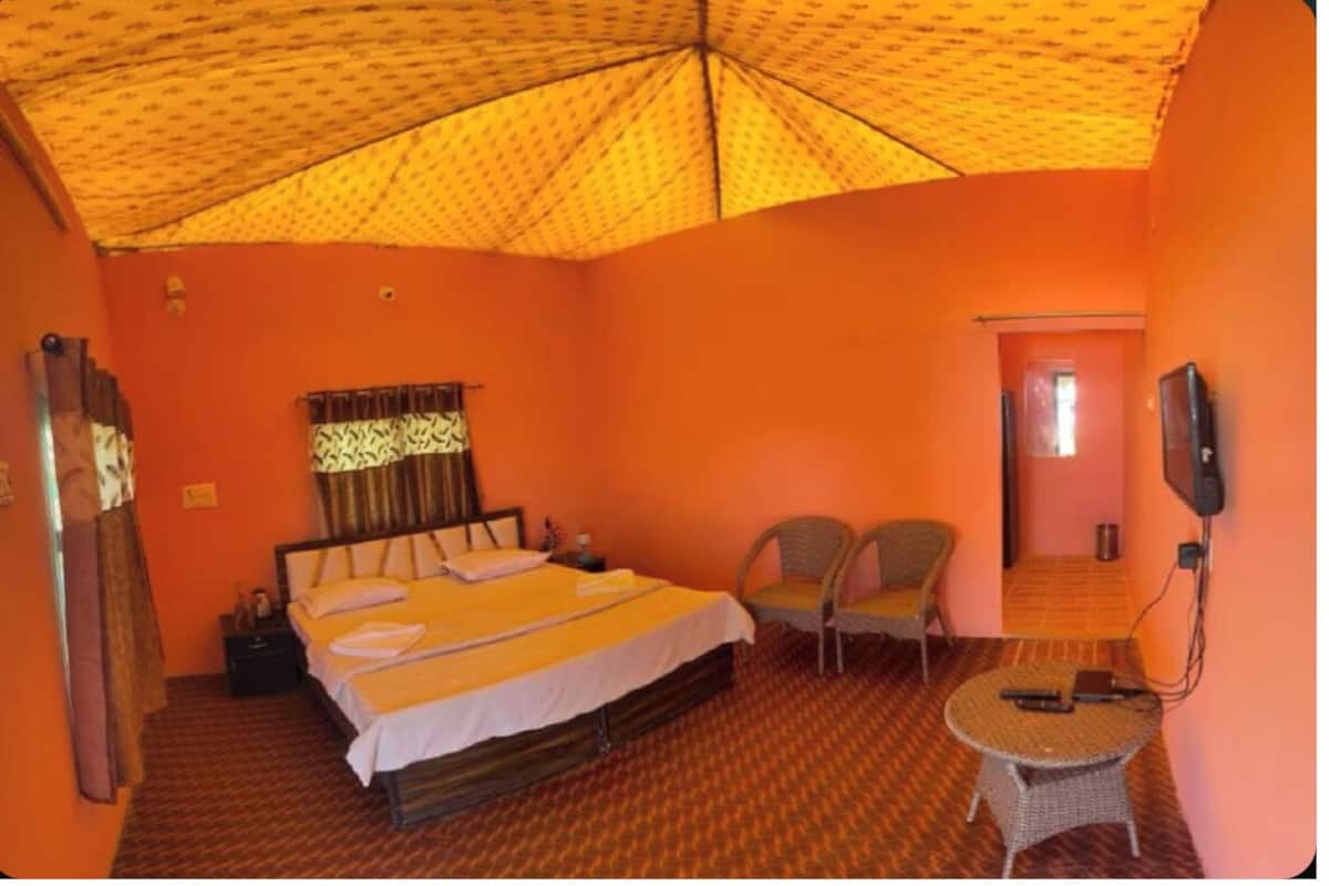 Una habitación con cama, dos sillas, una mesita, televisión y una puerta que da a otra estancia.
