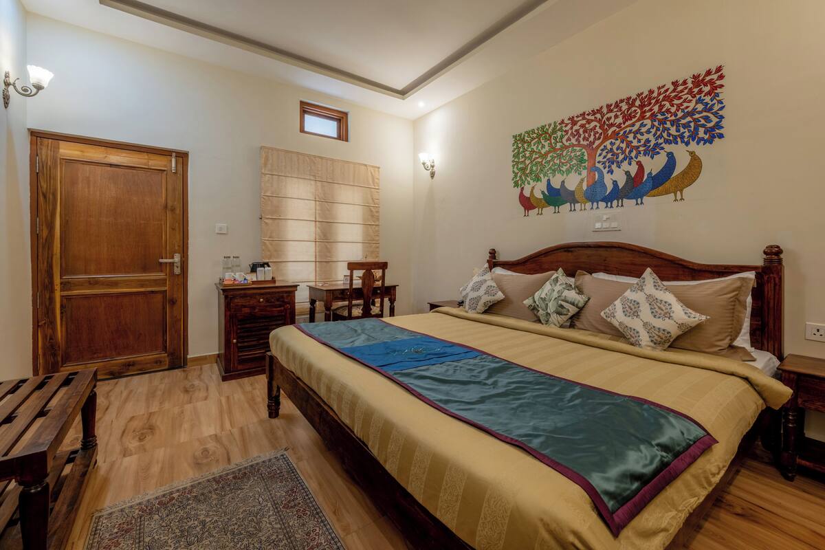 A bedroom with a wooden bed, a desk, a chair, a wooden wardrobe, and a wall-mounted shelf.